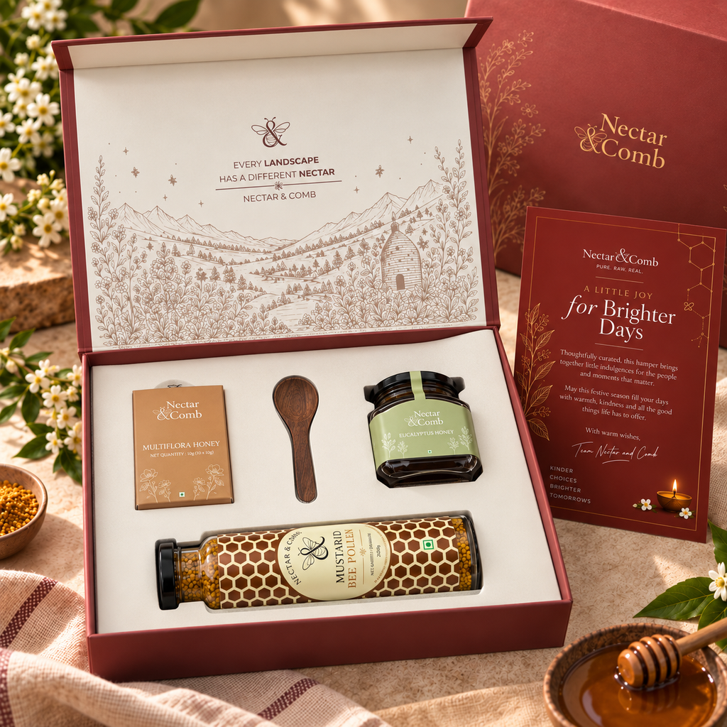 Nectar & Comb gift set displayed in an open burgundy box with illustrated interior, including a honey bottle, jar, small box, wooden spoon, and a card, styled on fabric with flowers and a honey dipper.