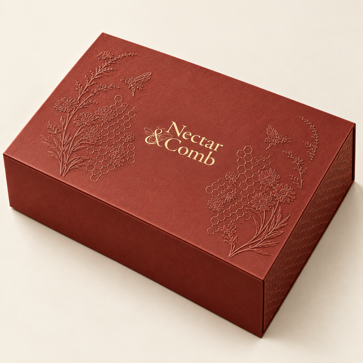 A rectangular red gift box with embossed floral and bee designs on the lid, featuring the brand name 'Nectar & Comb' in gold foil, set against a light beige background.