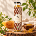 A glass jar of Mustar & Comb Mustard Bee Pollen granules stands on a wooden slice surrounded by honeycomb, small white flowers, and wooden bowls of pollen. The jar has a black lid and a label with a brown and white honeycomb pattern.