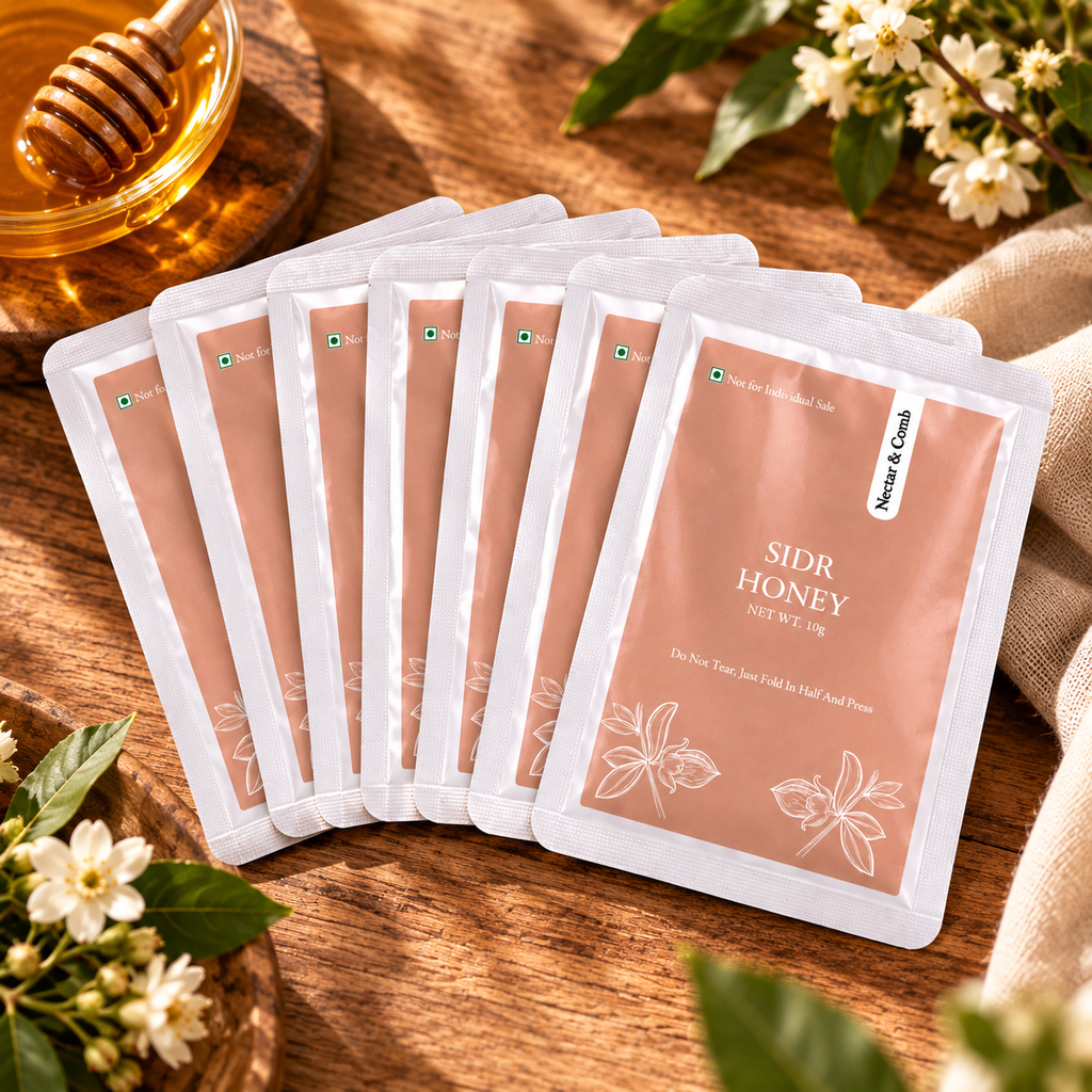 Six sachets of Sidr Honey are arranged in a fan shape on a rustic wooden surface, surrounded by decorative props including a honey dipper, honey jar, and small white flowers.