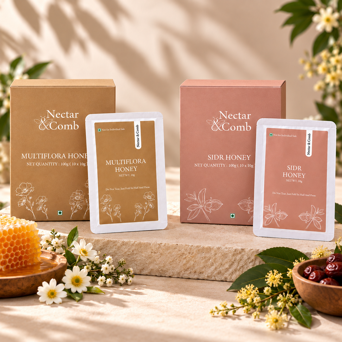 Two boxes and two sachets of Nectar & Comb honey products arranged on a stone slab with flowers, a honeycomb, and cherries in a styled studio setting.