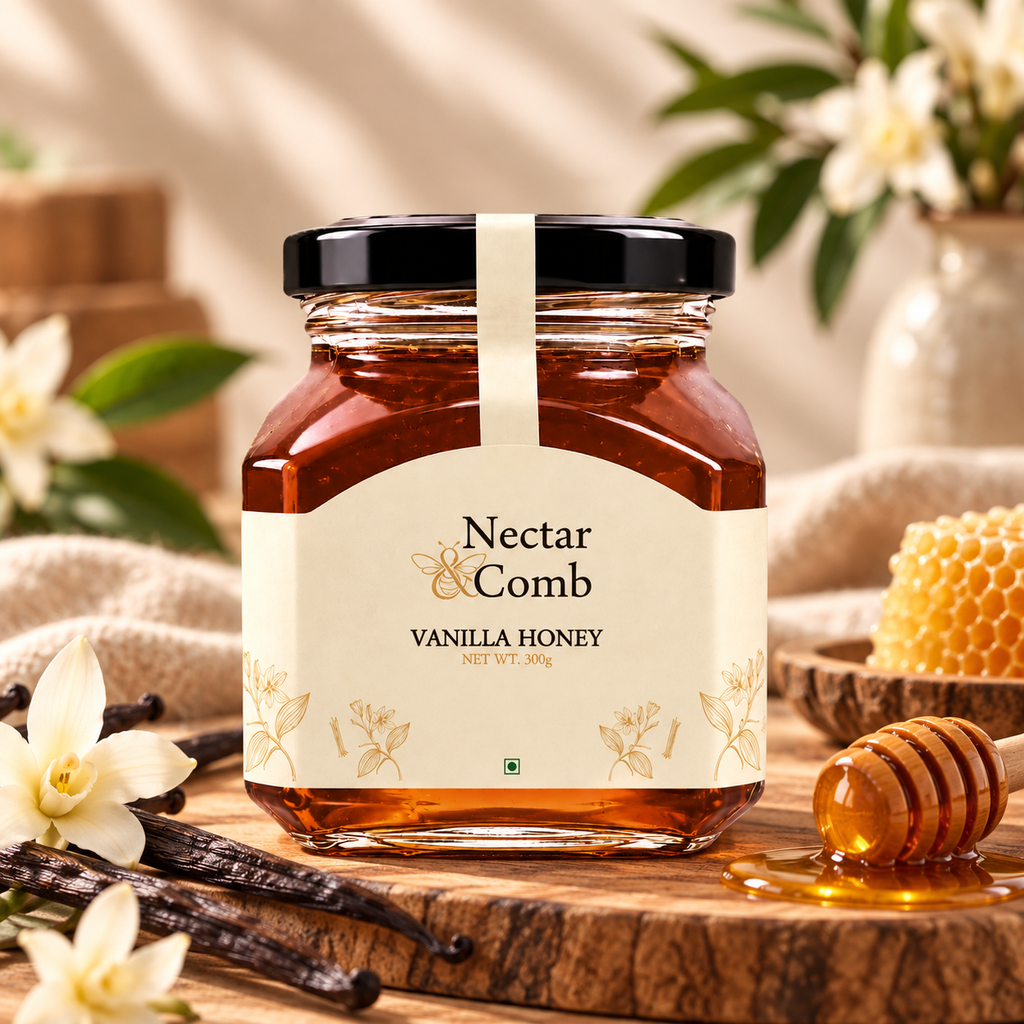 A jar of Nectar Comb Vanilla Honey centered on a wooden surface, surrounded by vanilla beans, white flowers, a honey dipper, and a honeycomb piece in a softly styled setting.