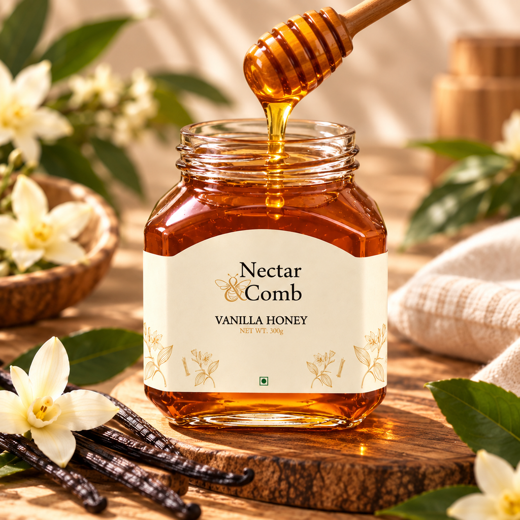 A glass jar of Nectar Comb Vanilla Honey sits on a wooden surface with honey dripping from a wooden dipper into the jar. The jar is surrounded by vanilla beans, white flowers, and green leaves on a rustic wooden background.